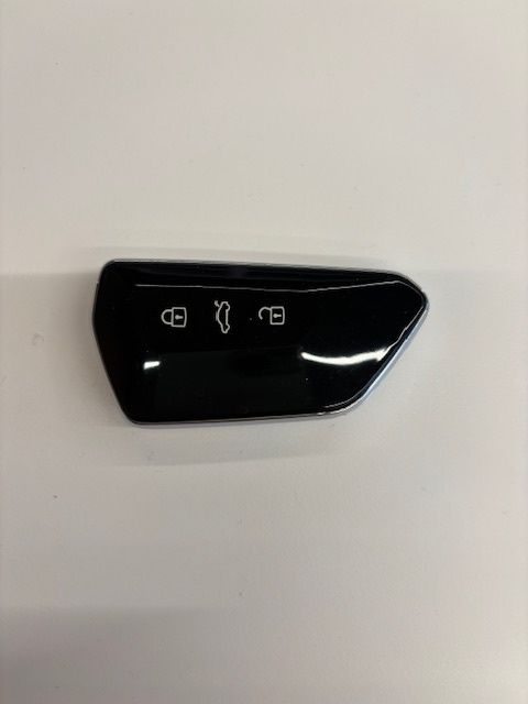 A black rectangular electronic component with a silver border. It has three white icons: a key, a car, and a lock. The key icon is on the left, the car icon is in the middle, and the lock icon is on the right.