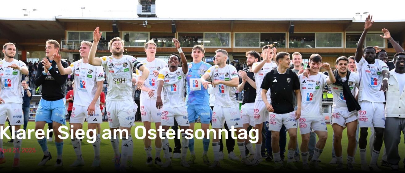Gruppe männlicher Fußballspieler feiert einen Sieg auf einem Rasenfeld. Sie tragen weiße Trikots mit verschiedenen Team-Logos. Der Text lautet 'm Ostersonntag'. Hinter ihnen ist ein verschwommener Hintergrund eines Gebäudes mit Glasfenstern und Menschen.