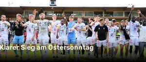 Gruppe männlicher Fußballspieler feiert einen Sieg auf einem Rasenfeld. Sie tragen weiße Trikots mit verschiedenen Team-Logos. Der Text lautet 'm Ostersonntag'. Hinter ihnen ist ein verschwommener Hintergrund eines Gebäudes mit Glasfenstern und Menschen.