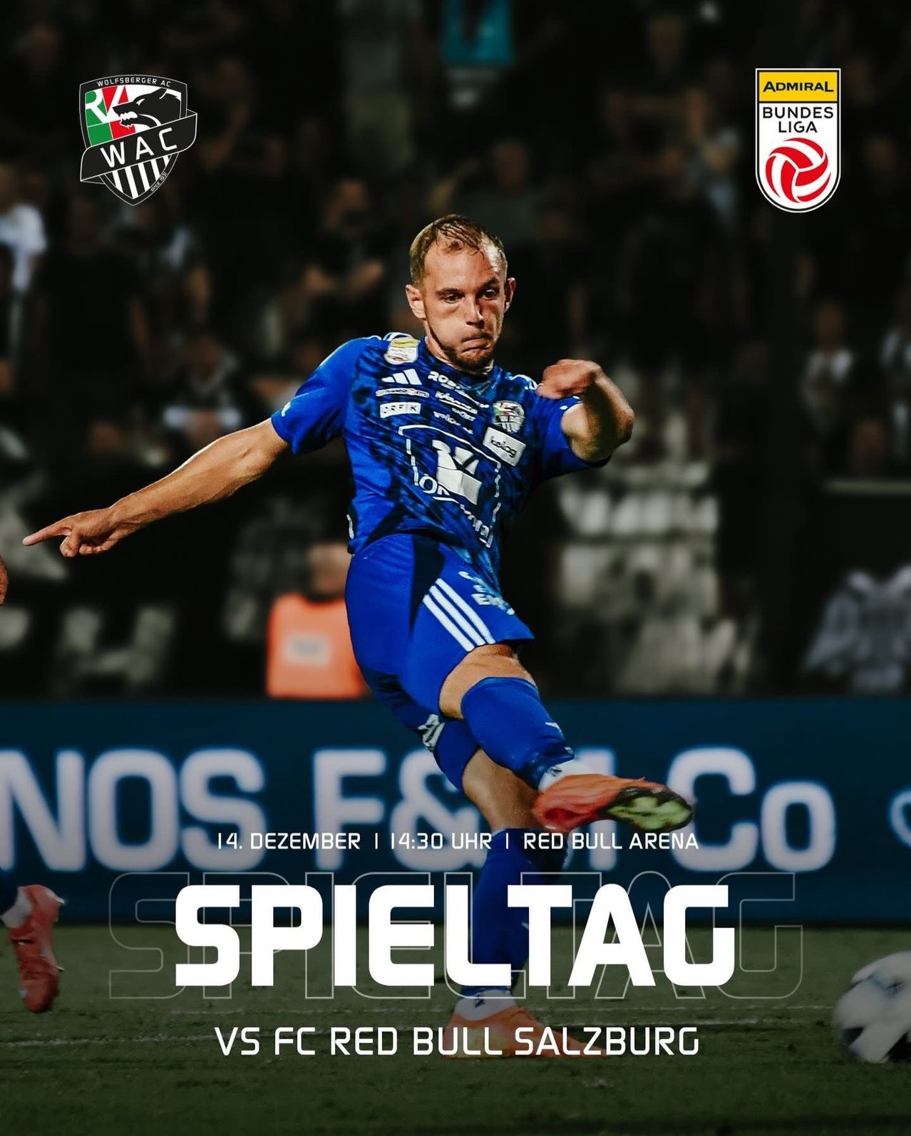 Fußballspieler in blauem Trikot tritt den Ball während eines Spiels. Datum und Uhrzeit des Spiels unten. Publikum im Hintergrund.