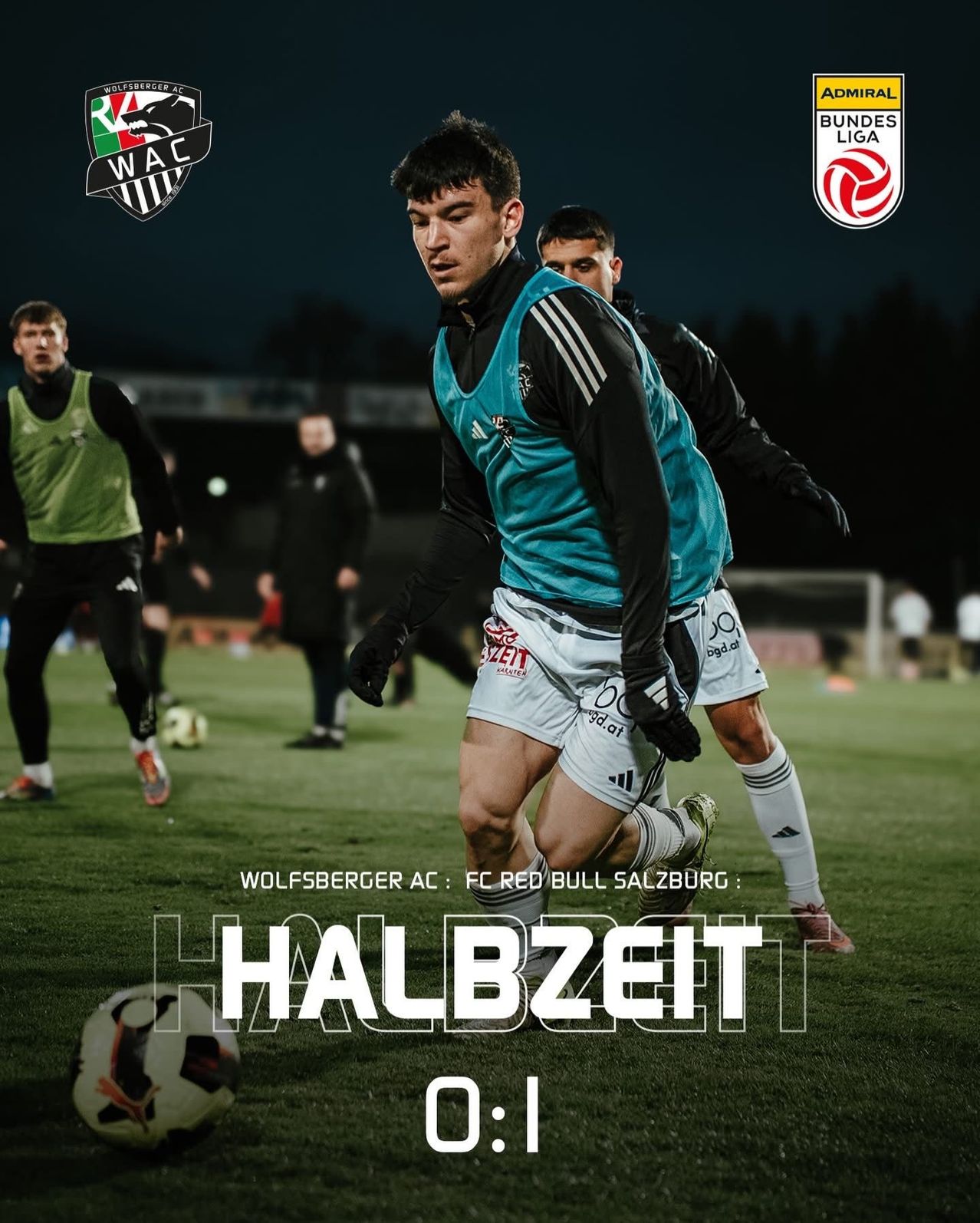 Fußballspieler sind auf dem Feld. Ein Spieler ist kurz davor, den Ball zu schießen. Ein anderer Spieler versucht, ihn zu blockieren. Dahinter steht ein Fußballtor.