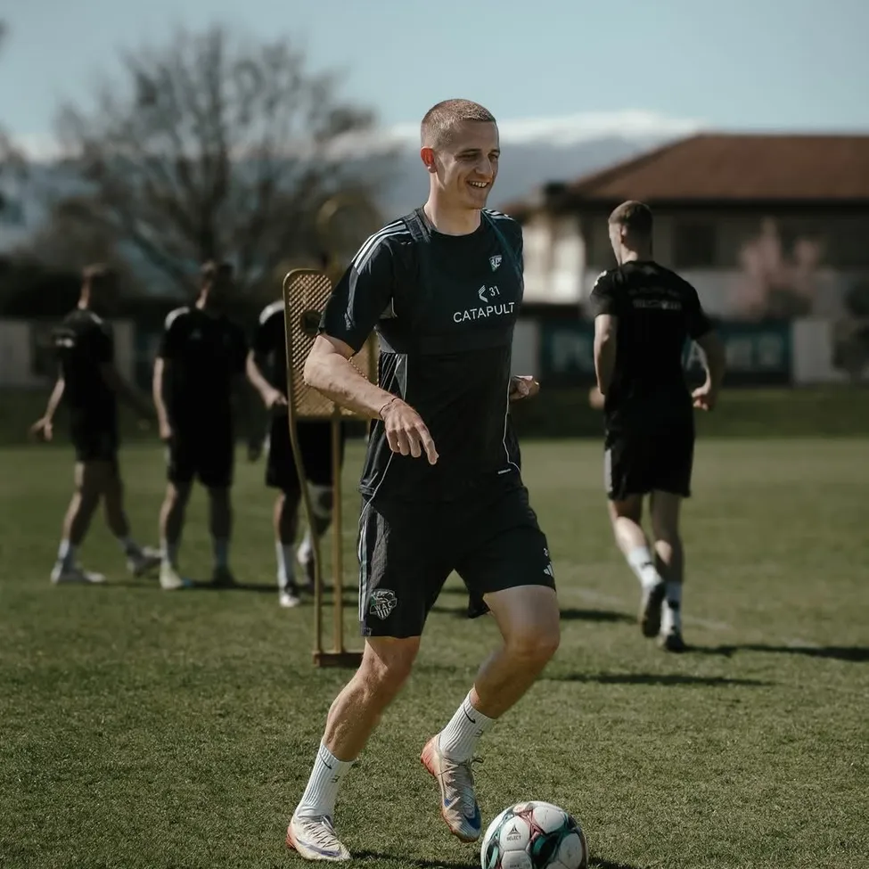 Ein Fußballspieler in einer schwarzen Uniform mit der Nummer 31 tritt einen Ball auf einem Feld, mit anderen im Hintergrund.