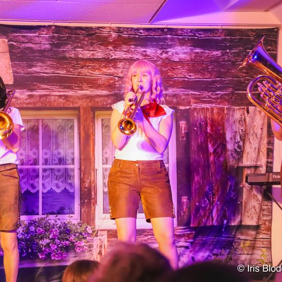 Bild enthält, Shorts, Adult, Female, Person, Woman, Brass Section, Horn, Musical Instrument, Group Performance, Face