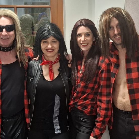 Vier Menschen posieren für ein Foto; zwei Männer und zwei Frauen. Sie tragen alle rote und schwarze karierte Langarmhemden. Die Frau in der Mitte trägt eine schwarze Lederjacke.