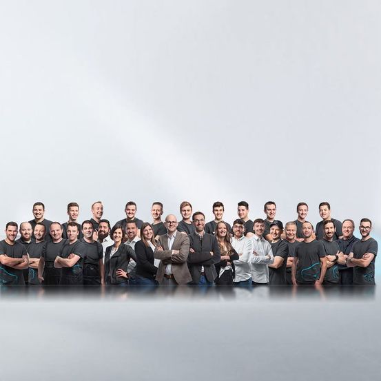 Eine Gruppe von Menschen, gekleidet in Schwarz, posiert für ein Foto. Einige tragen Brillen und einige tragen Hüte. Der Hintergrund ist grau.