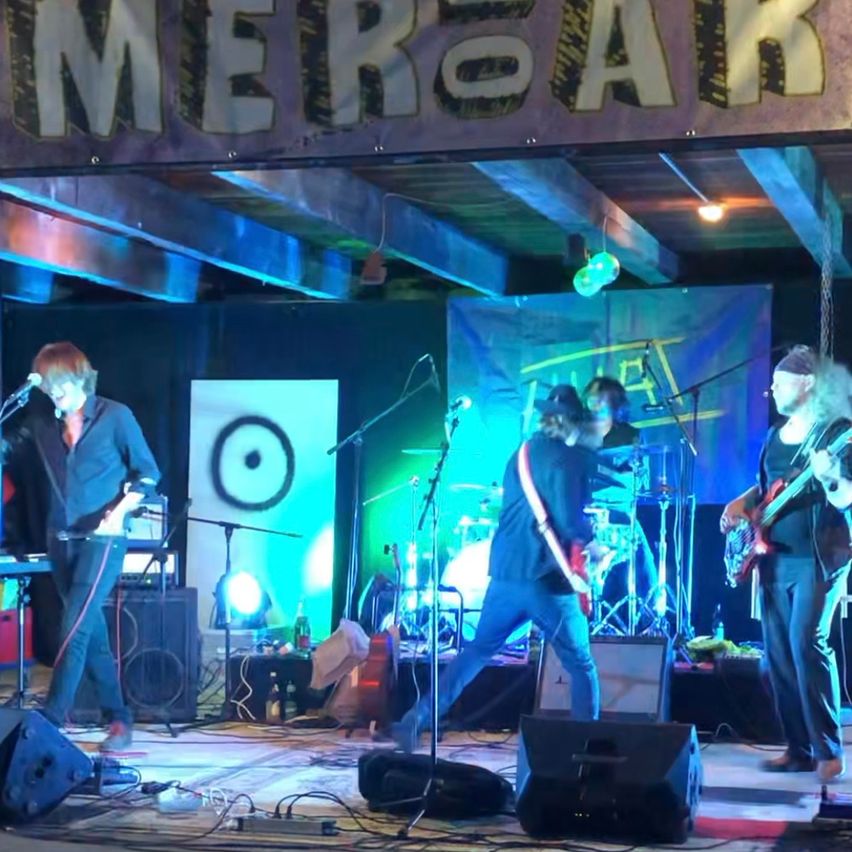 A band performs on stage with a banner reading 'MERBAR' above them. The stage is lit with green and blue lights.