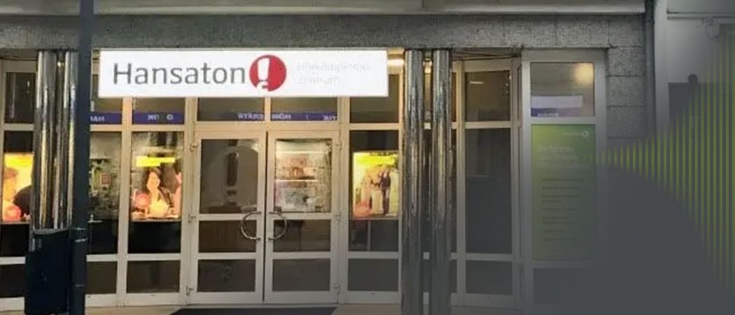 Ein Gebäudeeingang zeigt ein Schild mit dem Wort 'sation' über den Türen. Die Türen sind aus Glas mit Metallgriffen. Ein Poster befindet sich an der Wand neben den Türen.