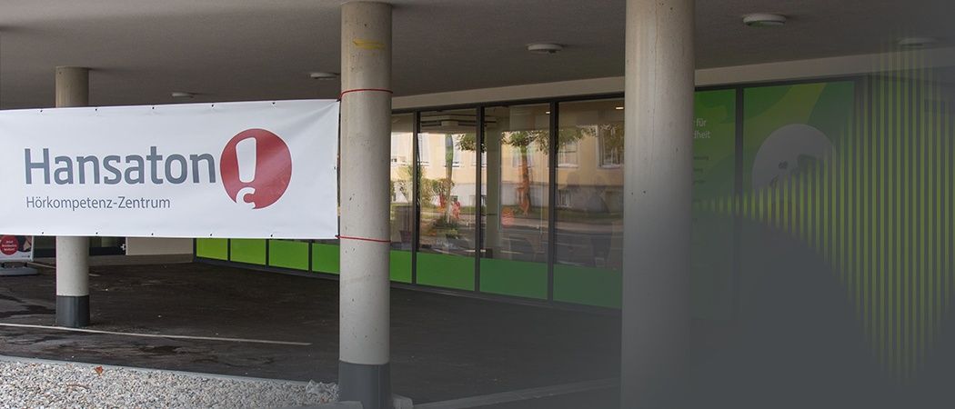 Ein Gebäude mit einem roten und weißen Banner, das 'on!' schreibt. Grüne und weiße Wände, Glasfenster mit Reflexionen eines Baumes und eines Autos.