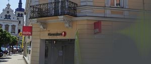 Ein Gebäude mit Balkon und Schild, das 'Hansaton', ein rotes Schild 'BIPA' und eine grüne Fahne zeigt.