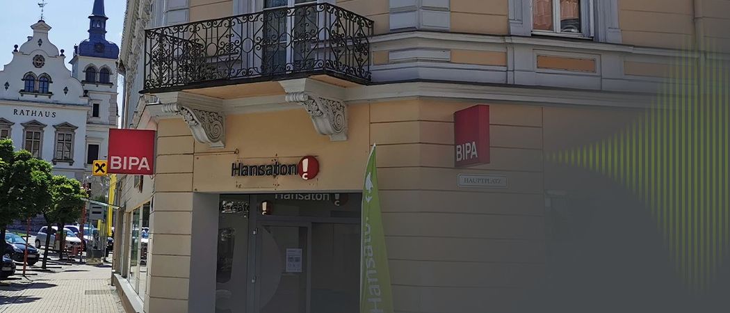 Ein Gebäude mit Balkon und Schild, das 'Hansaton', ein rotes Schild 'BIPA' und eine grüne Fahne zeigt.