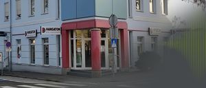 Ein Ladengeschäft mit einem Schild, das 'HANSATON Horsysteme' auf einem mehrstöckigen Gebäude anzeigt. Es gibt Glastüren und Fenster sowie ein blaues Fußgängerübergangsschild.