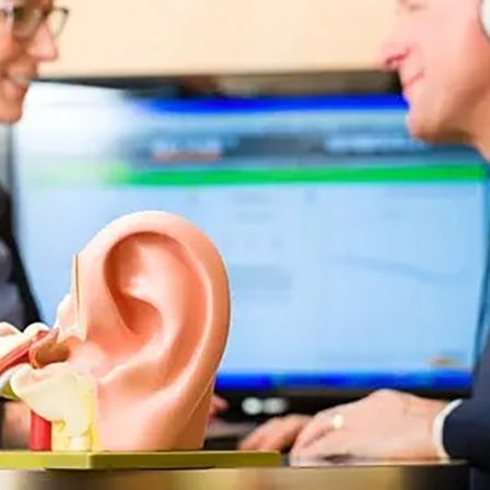 Ein Mann und eine Frau betrachten ein 3D-Ohrmodell mit Kopfhörern. Sie lächeln und sitzen vor einem Computerbildschirm.