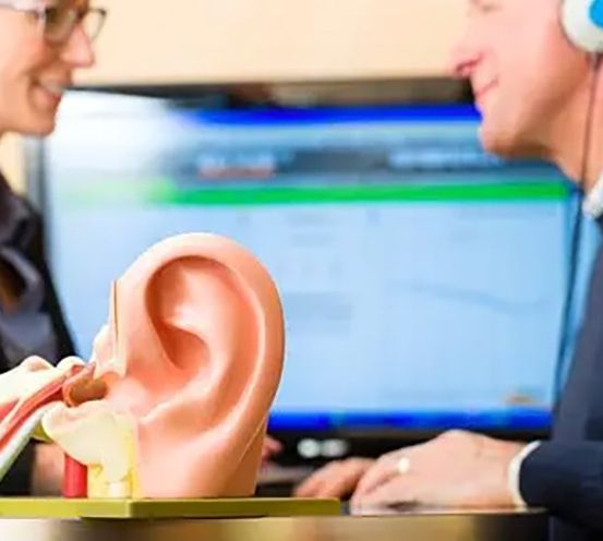 Ein Mann und eine Frau betrachten ein 3D-Ohrmodell mit Kopfhörern. Sie lächeln und sitzen vor einem Computerbildschirm.