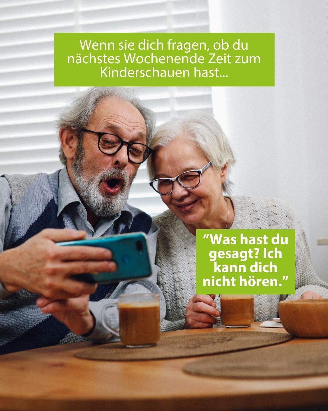 Zwei ältere Menschen sitzen an einem Tisch, lächeln und halten Kaffeetassen. Einer schaut auf sein Handy, während der andere eine Brille trägt und ihn ansieht. Eine grüne Sprechblase mit deutschem Text ist in der Mitte.
