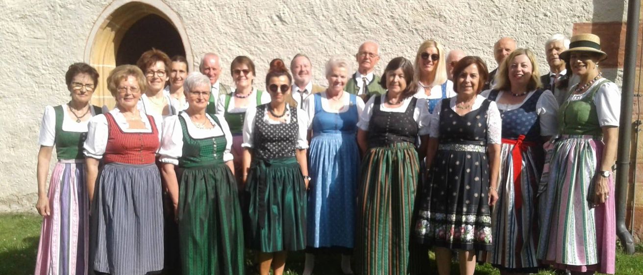 Eine Gruppe von Menschen in traditioneller Kleidung, wahrscheinlich für ein Fest, posiert für ein Foto vor einem Gebäude.