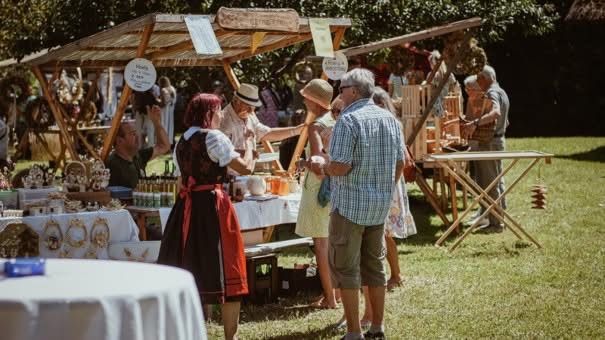 Eine Gruppe von Menschen kauft auf einem Freiluftmarkt ein, wo Stände verschiedene Artikel verkaufen. Einige tragen Hüte und Brillen.