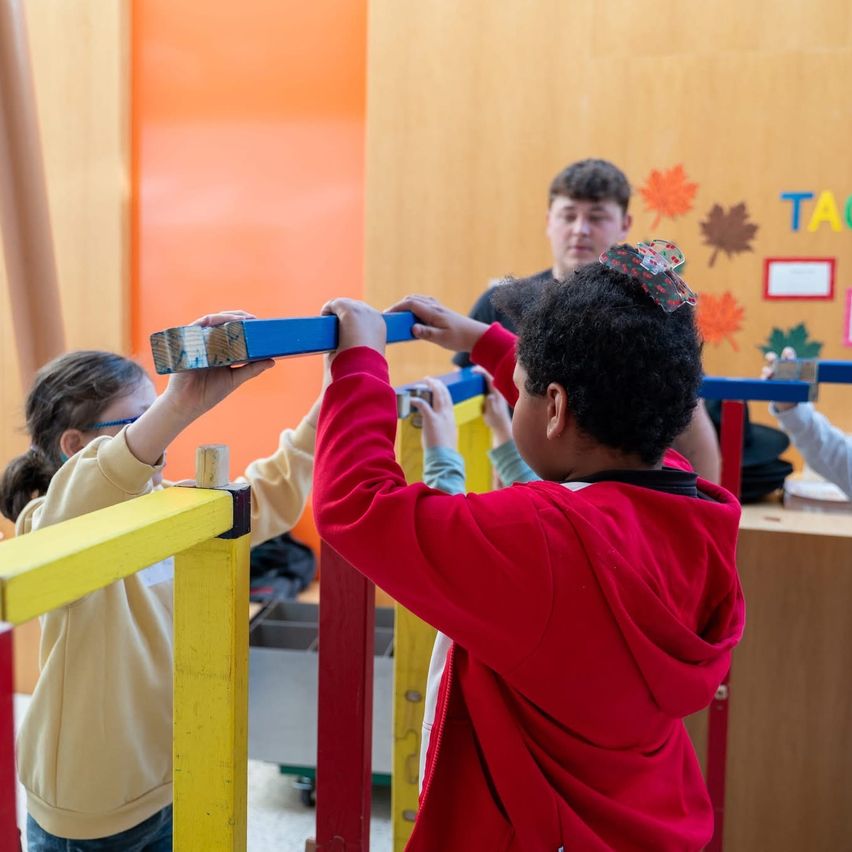 Zwei Kinder spielen mit einer blauen und gelben Struktur in einem Spielzimmer. Ein Kind hält ein blaues Stück, während das andere ein gelbes Stück hält.