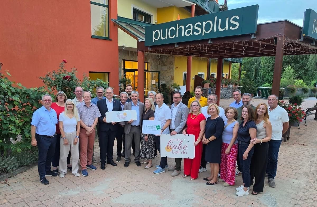 Eine Gruppe von Menschen steht vor einem Gebäude mit dem Schild 'puchaplus' über ihnen. Sie halten Schilder mit den Worten 'Lauta liabe Lei do' in den Händen.