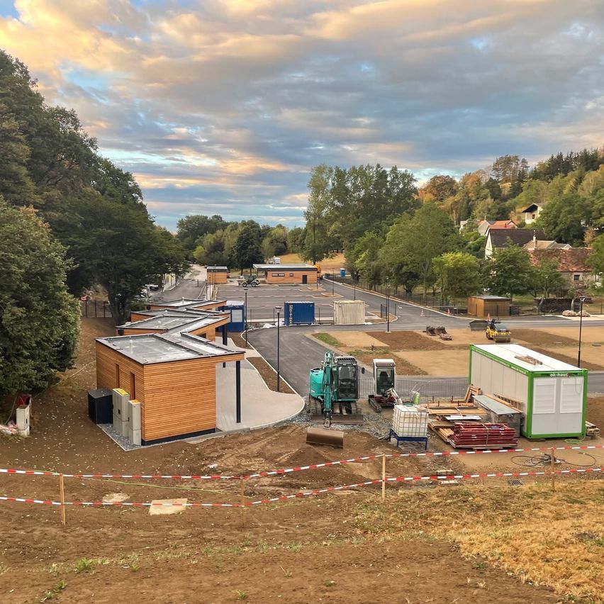 A construction site with several wooden structures, machinery, and a road under a cloudy sky.