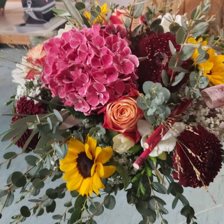 A vibrant bouquet with pink hydrangeas, red roses, yellow sunflowers, and green leaves. The arrangement is colorful and well-composed.
