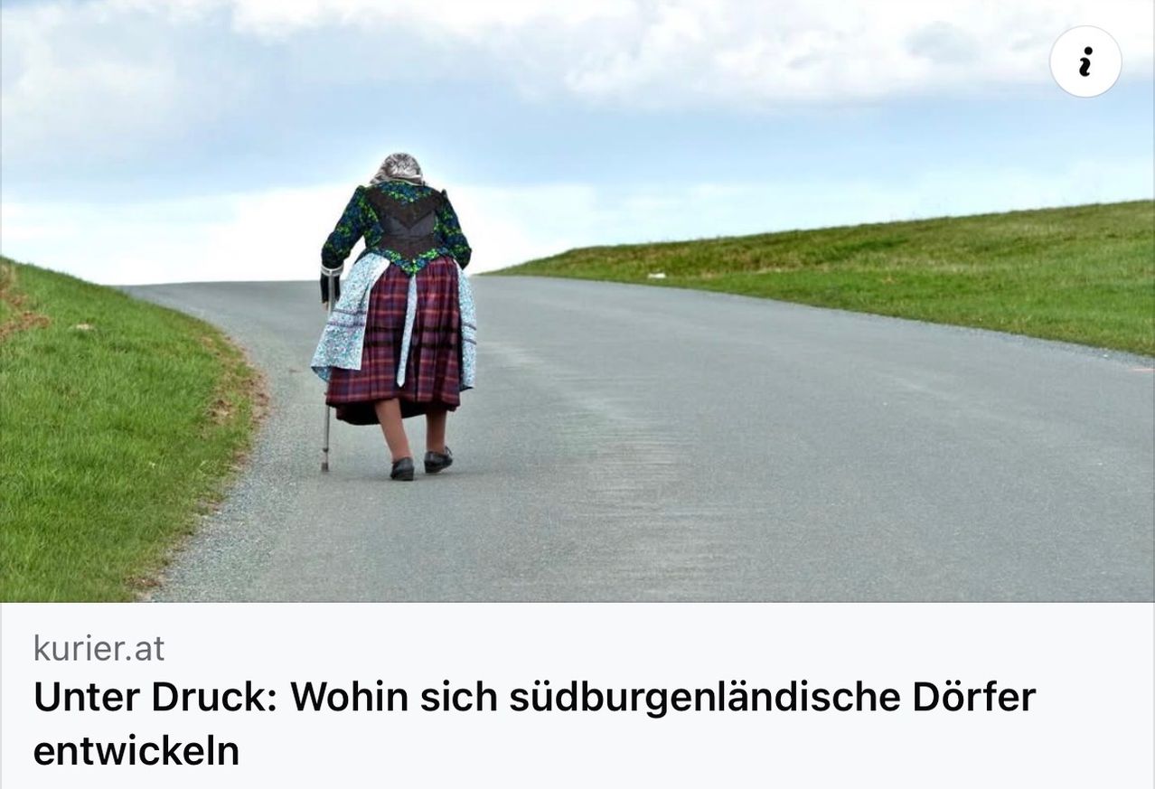 An elderly woman walks down a road in traditional clothing with a cane. The background features a hill and a blue sky with clouds.