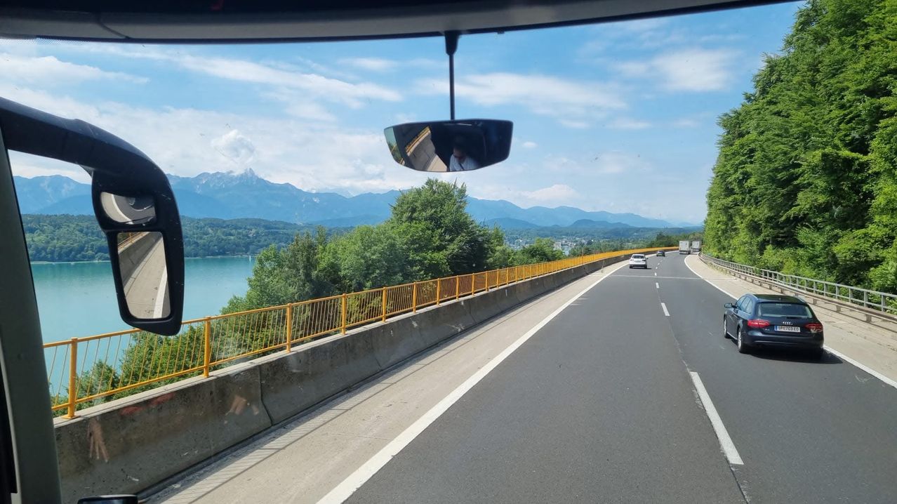 A highway view with cars driving, mountains in the background, and a lake to the left.