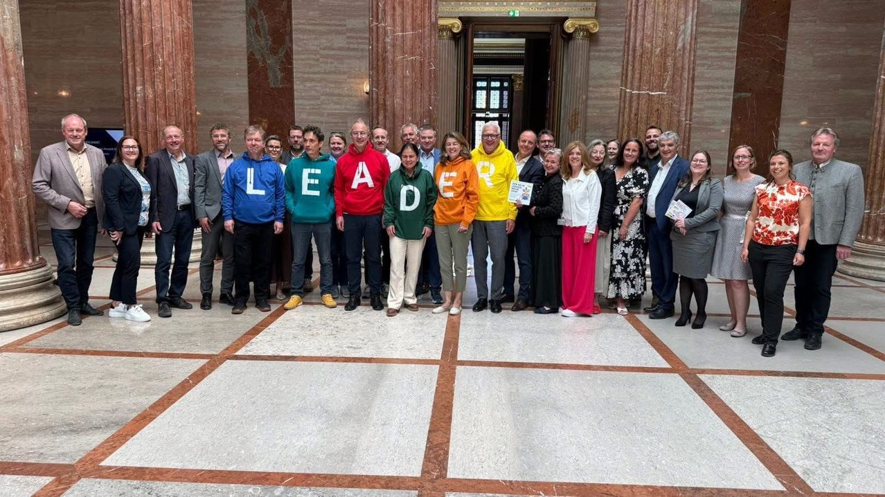 Eine Gruppe von Menschen steht vor einem Gebäude, sie tragen Pullover und Jacken. Sie lächeln und scheinen für ein Foto zu posieren.