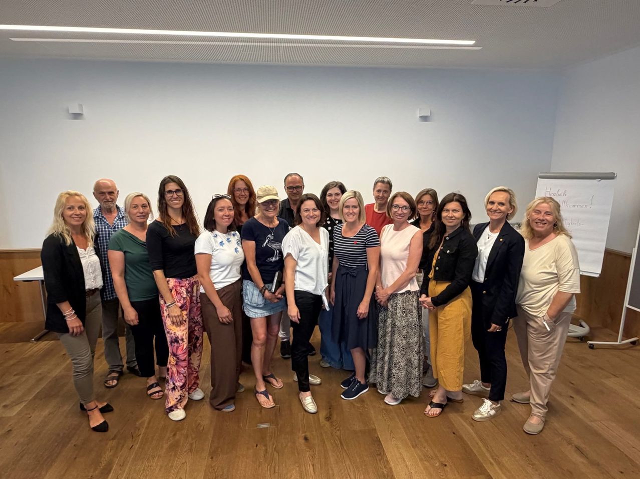 Gruppe von 22 Personen steht in einem Raum vor einer weißen Wand und einem Flipchart.
