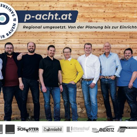 Sieben Männer stehen vor einer Holzwand, lächeln und posieren für ein Foto. Sie tragen Freizeitkleidung, und ihre Schatten fallen auf die Wand. Der Text lautet 'Regional umgesetzt. Von der Planung bis zur Einrichtung.'