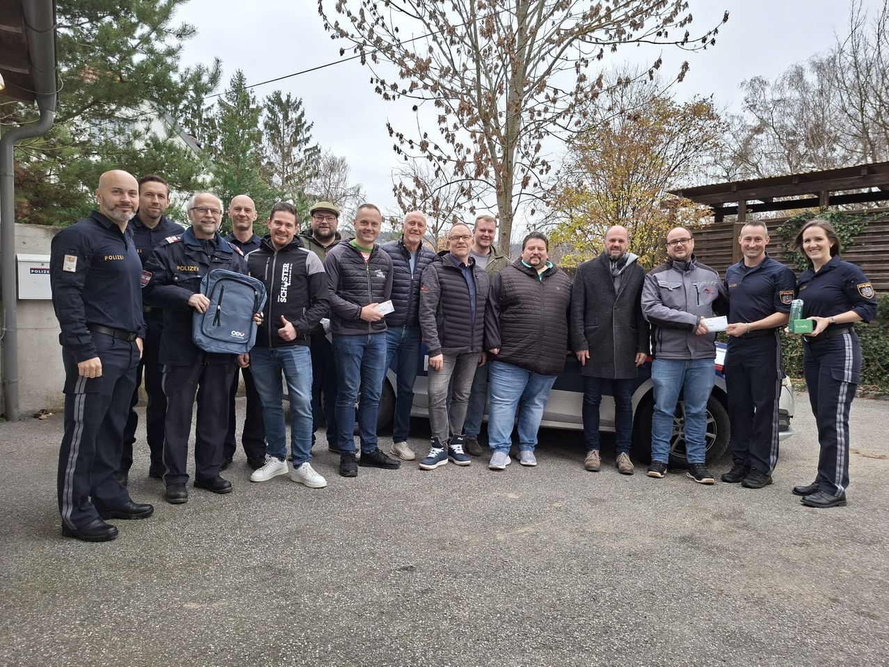 Eine Gruppe von Männern in Uniformen posiert für ein Foto vor einem Polizeiauto. Sie lächeln und scheinen etwas zu erhalten.