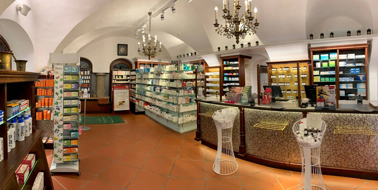 Ein gut beleuchteter Innenraum eines Boutique-Ladens mit Regalen voller verschiedener Produkte, einer Kronleuchter und einer Theke mit einem Korb voller Artikel.