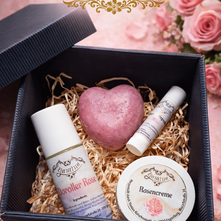 Eine schwarze Box mit einem herzförmigen Badeseife und zwei kosmetischen Produkten. Die Box ist mit Stroh gefüllt und hat einen dekorativen Blumenhintergrund.