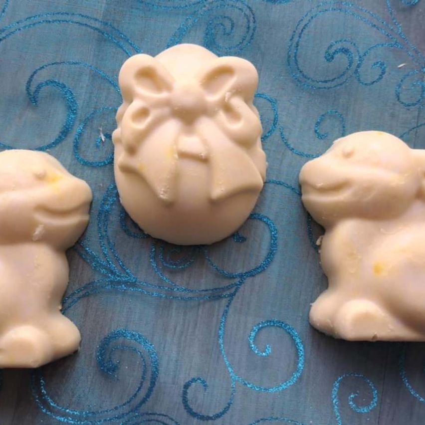 Drei weiße Seifen in Form von Mäusen liegen auf einem blauen Tuch mit Schwüngen. Die in der Mitte hat einen Bogen auf dem Kopf.