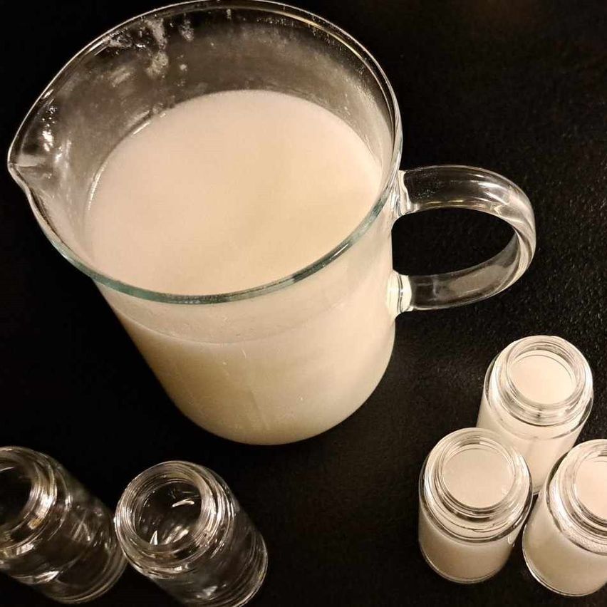 Ein Krug mit weißer Creme steht auf einer schwarzen Oberfläche neben vier kleinen Glasgläsern.