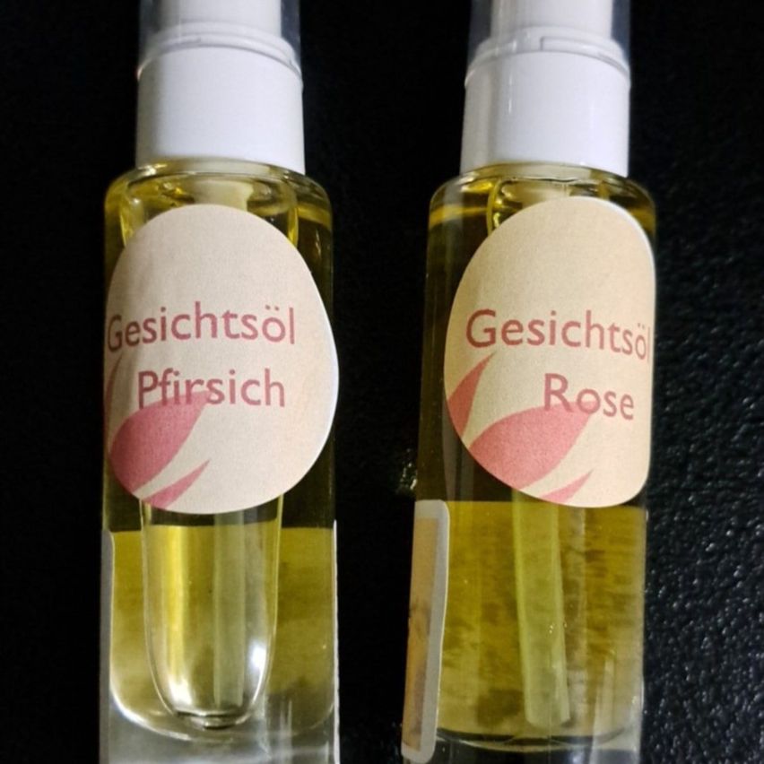 Zwei Flaschen Gesichtsöl mit Etiketten, die 'Gesichtsöl Pfirsch' und 'Gesichtsöl Rose' lesen, beide auf schwarzem Hintergrund.