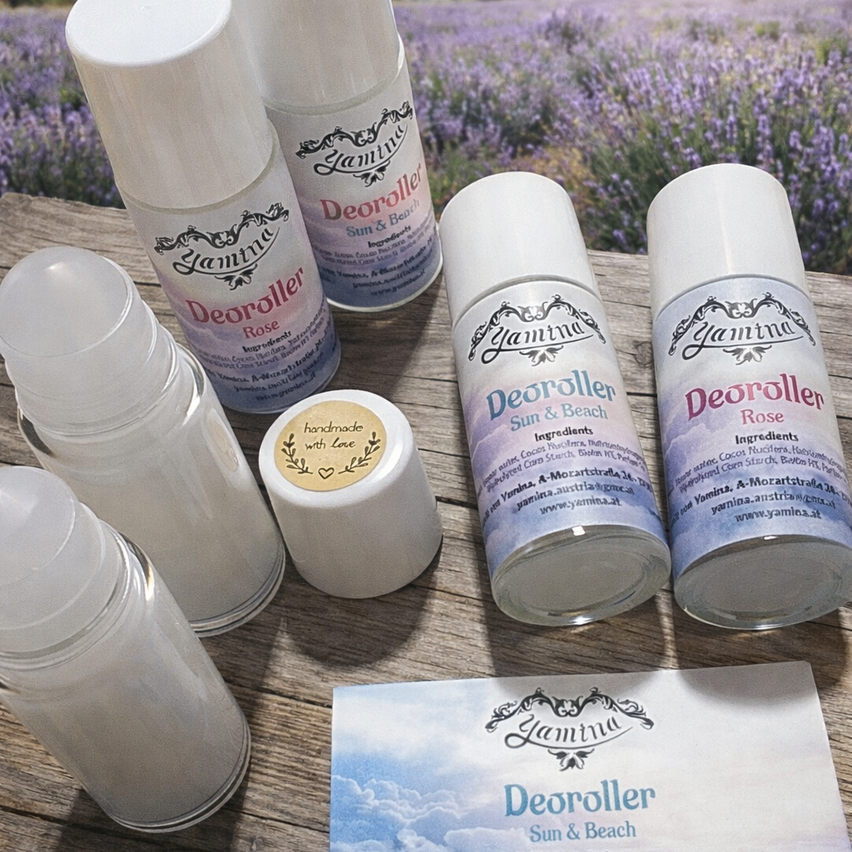 Six deodorizer bottles are on a wooden table. A few bottles are labeled Deoroller Rose and Sun & Beach. A small card with the same label is also on the table.
