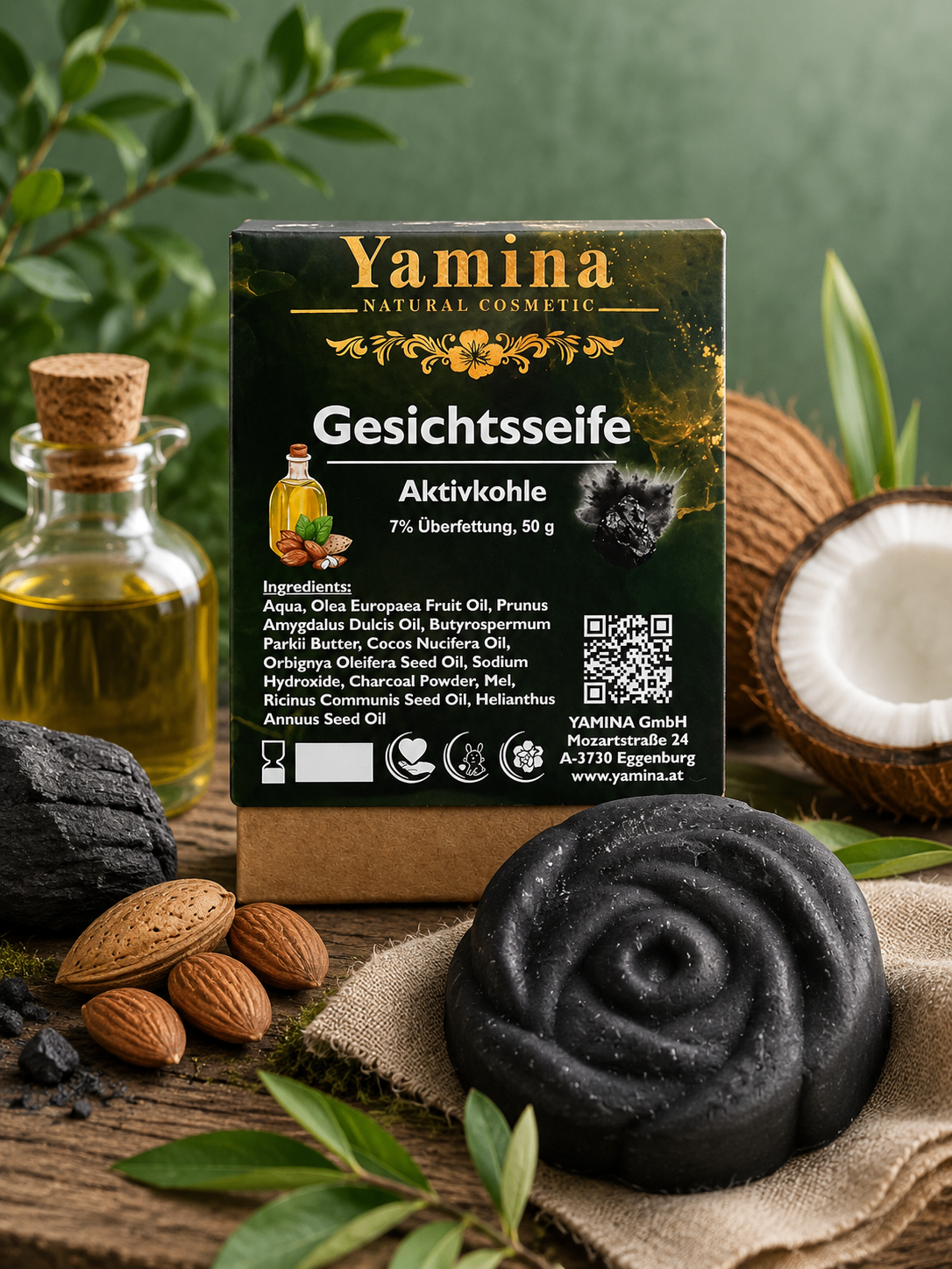 Eine Schachtel Yamina natürliches kosmetisches Gesichtsseife mit Aktivkohle, 7% Ölgehalt, 50g, präsentiert mit einer Flasche Öl, Kokosnuss und Mandeln.