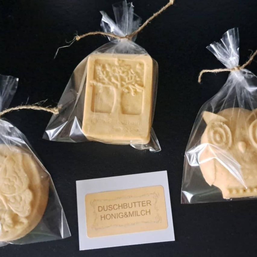 Four soaps in plastic bags with tree, owl, and other designs, with a label reading 'Duschbutter Honig&Milch'.