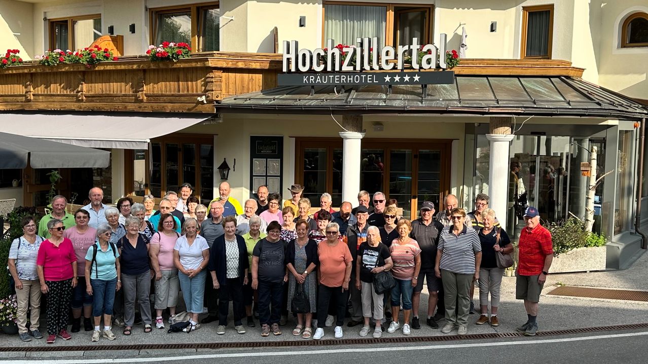 Eine Gruppe älterer Menschen steht vor einem Hotel namens Hochzillertal. Sie alle lächeln und posieren für ein Foto.