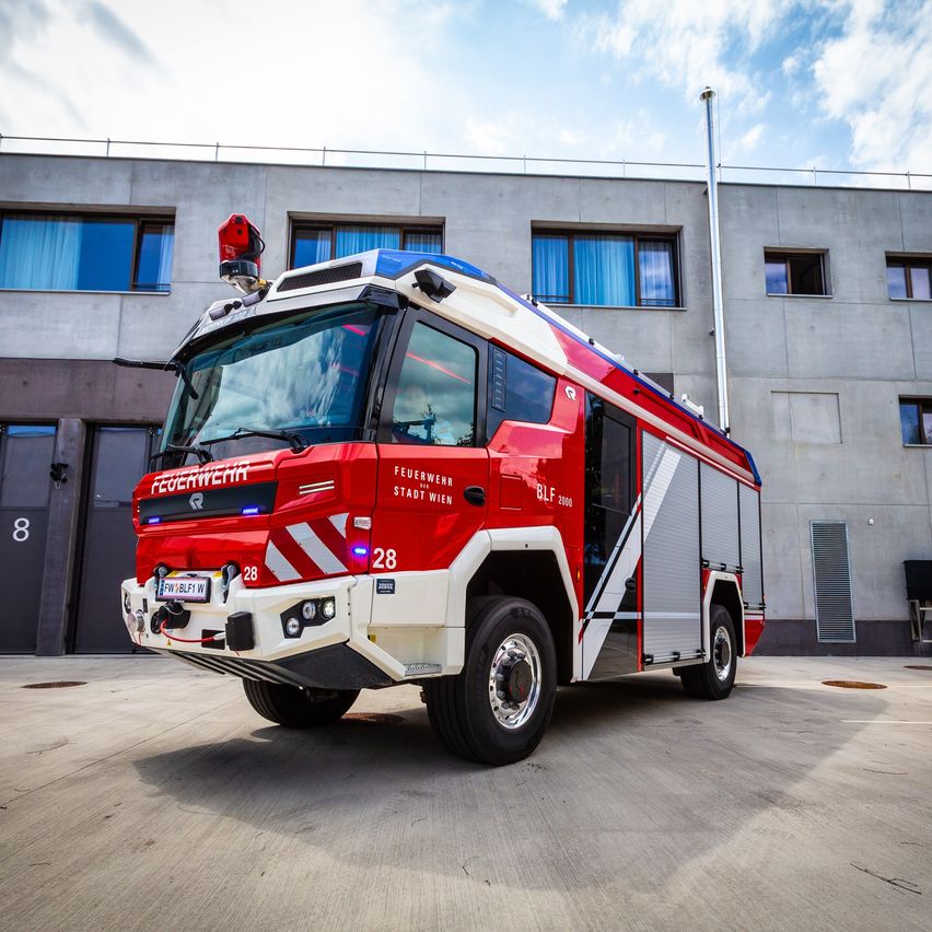 Ein roter und weißer Feuerwehrwagen mit der Aufschrift Feuerwehr Stadt Wien steht vor einem Gebäude. Der Wagen hat seine Türen geöffnet und ist mit der Nummer 28 gekennzeichnet.