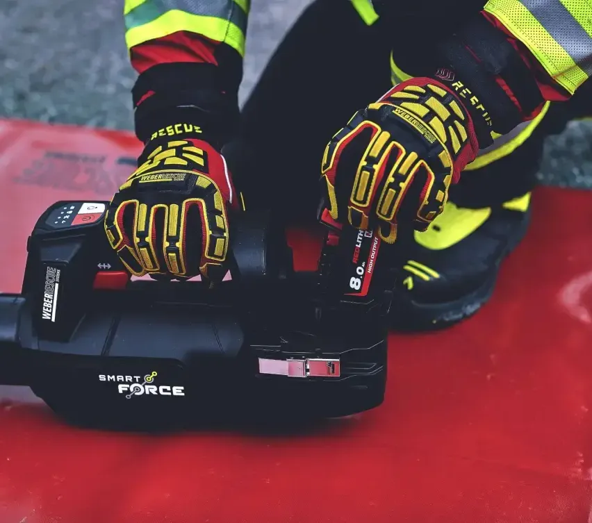 Ein Feuerwehrmann in Spezialausrüstung kniet und hält ein schwarzes Gerät mit der Aufschrift 'SMART FORCE'. Die Szene spielt sich auf einer roten Fläche ab.