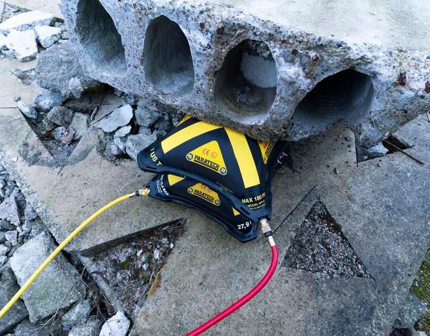 Ein Paratech-Werkzeug ruht auf einem Haufen Steine mit einem roten Schlauch, der daran angeschlossen ist, und zeigt ein Detail seines gelben und schwarzen Designs.