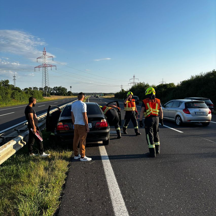 Zwei Personen stehen neben einem Auto am Straßenrand. Vier Personen sind auf der Straße, zwei sind Feuerwehrleute und zwei versuchen, dem Auto zu helfen.