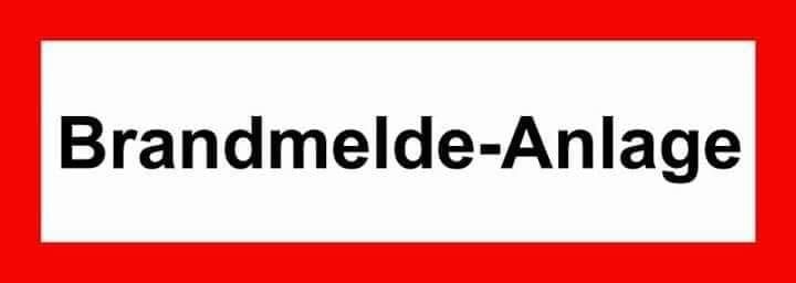 Ein weißes rechteckiges Schild mit roten Rändern zeigt schwarzen Text, der 'Brandmelde-Anlage' lautet.