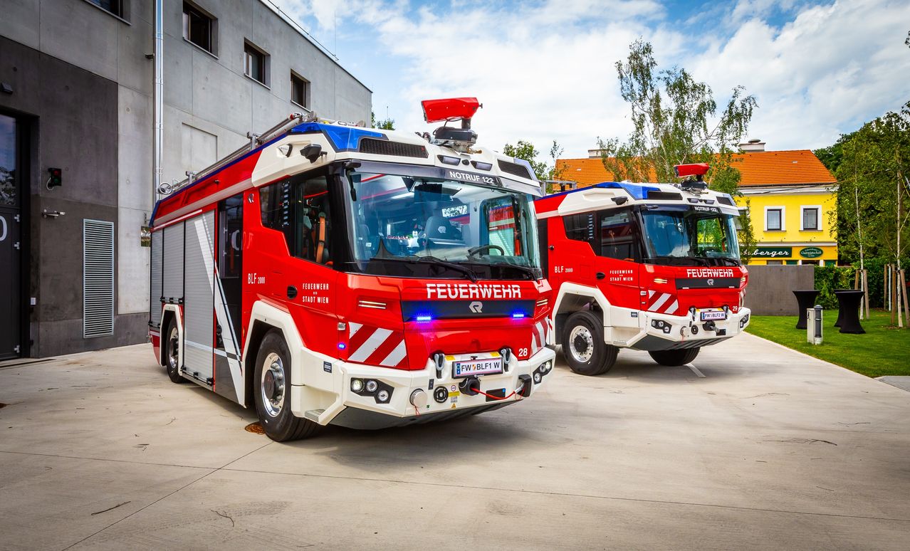 Zwei Feuerwehrfahrzeuge sind nebeneinander geparkt. Eines ist mit 'BLF 2000' und das andere mit 'FEUERWEHR' beschriftet. Beide haben rote und weiße Streifen.