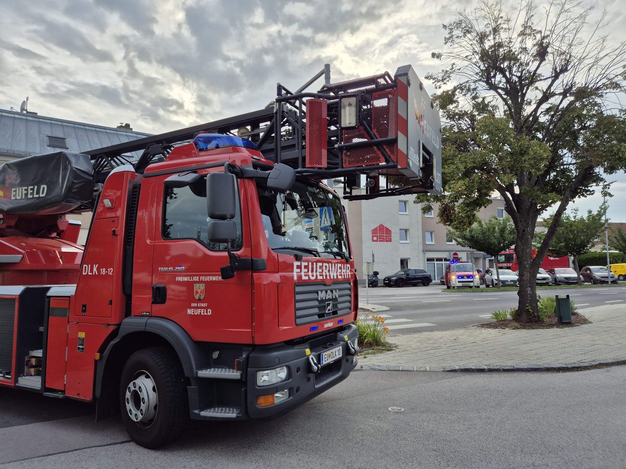 Ein roter Feuerwehrwagen ist auf der Straße geparkt, mit einer großen Leiter obenauf. Der Wagen ist mit 'Feuerwehr' und Neufeld gekennzeichnet.