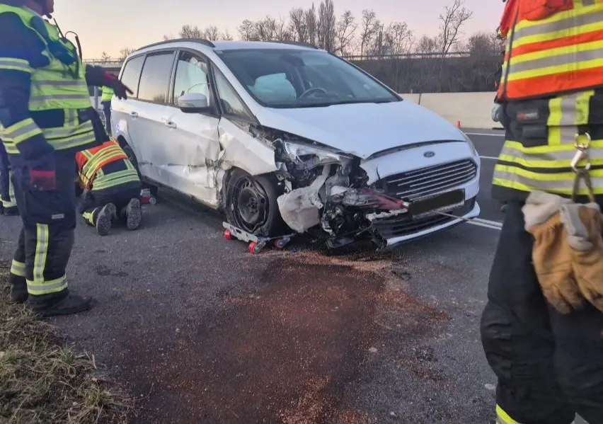 Ein weißer Ford-Wagen mit erheblichen Frontschäden steht am Straßenrand. Rettungskräfte sind anwesend und begutachten den Schaden.