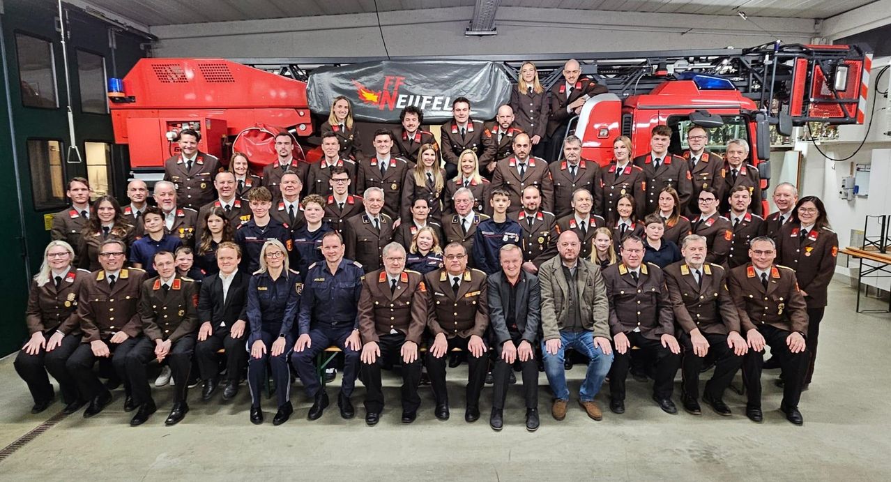 Eine Gruppe von Menschen in Uniform und formeller Kleidung posiert für ein Foto vor einem Feuerwehrauto.