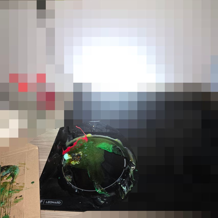 Ein Bild von einer zerbrochenen Keramikschüssel, gefüllt mit grüner und roter Farbe, auf einer schwarzen Oberfläche, möglicherweise einem Tisch, mit einem Karton in der Nähe.