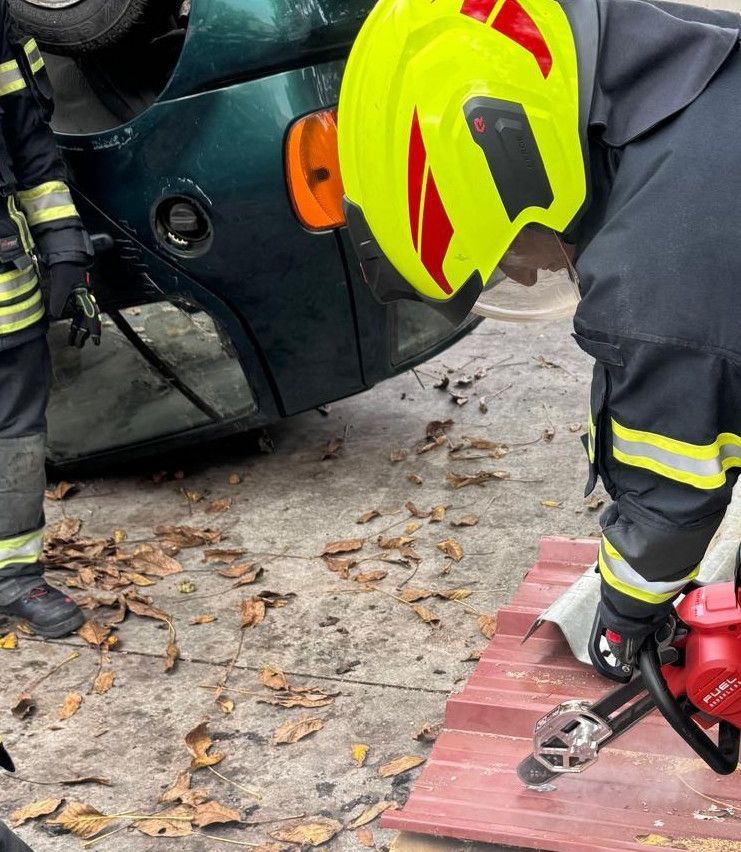 Feuerwehrleute in voller Ausrüstung arbeiten am Heck eines beschädigten Fahrzeugs und entfernen mit einer roten Kettensäge Schmutz.